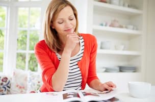 woman in an orange cardigan and striped top reading a magazine 