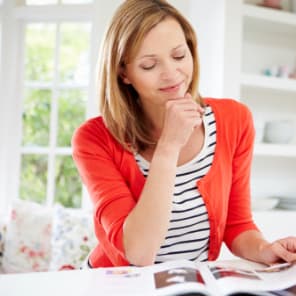 woman in an orange cardigan and striped top reading a magazine 